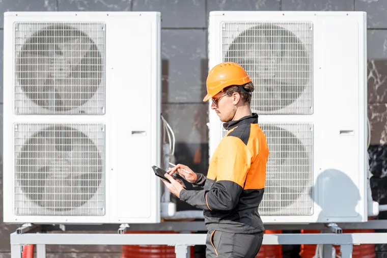 HVAC technician using a tablet while servicing outdoor equipment